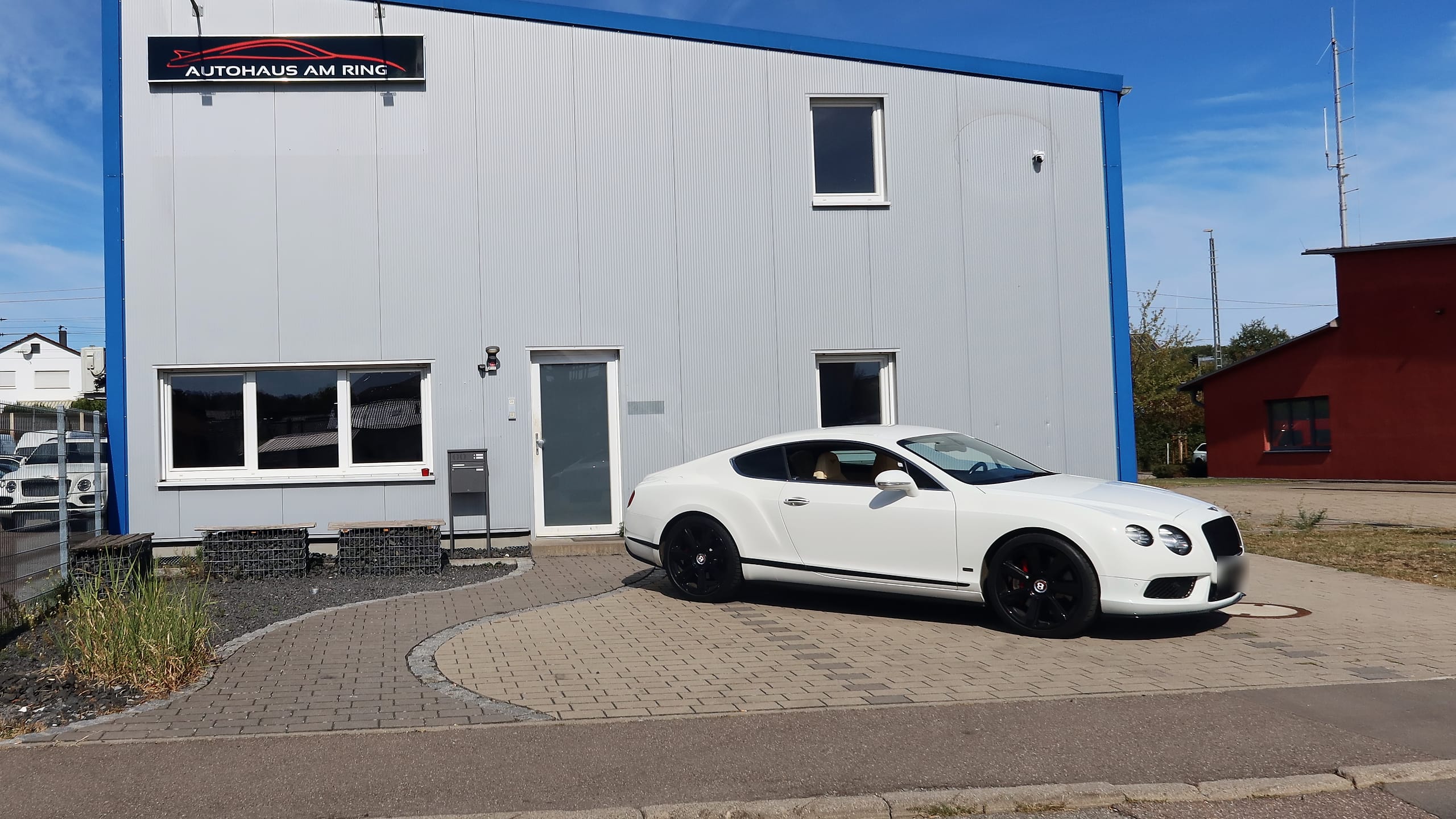 Die Halle des Autohauses am Ring an der Luigstraße mit dem Schild oben an der Fassade, davor ein weißer Bentley