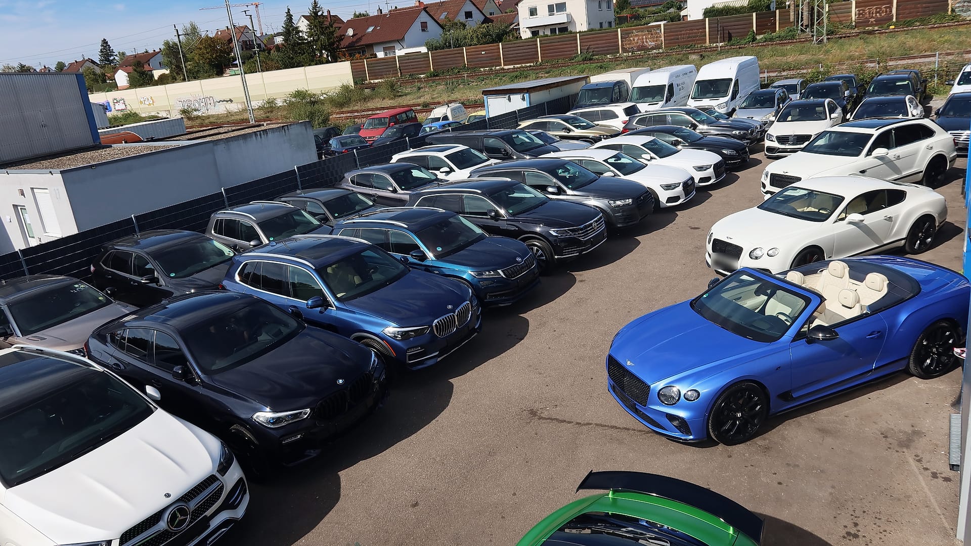 Blick von oben auf den Hof mit Fahrzeugreihen, vorn rechts ein blaues Bentley Cabrio