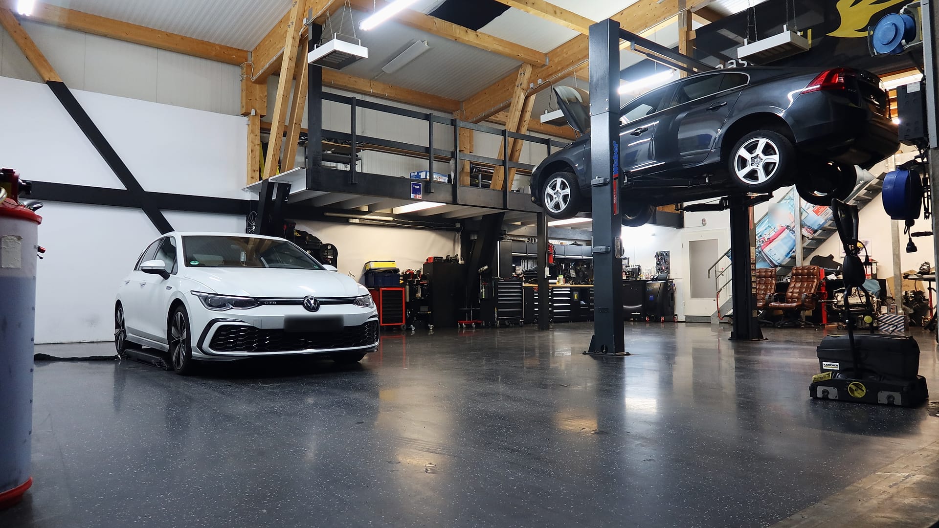 Die Werkstatthalle mit Holzdach und Empore: ein Fahrzeug auf der Hebebühne, davor ein weißer VW Golf GTD
