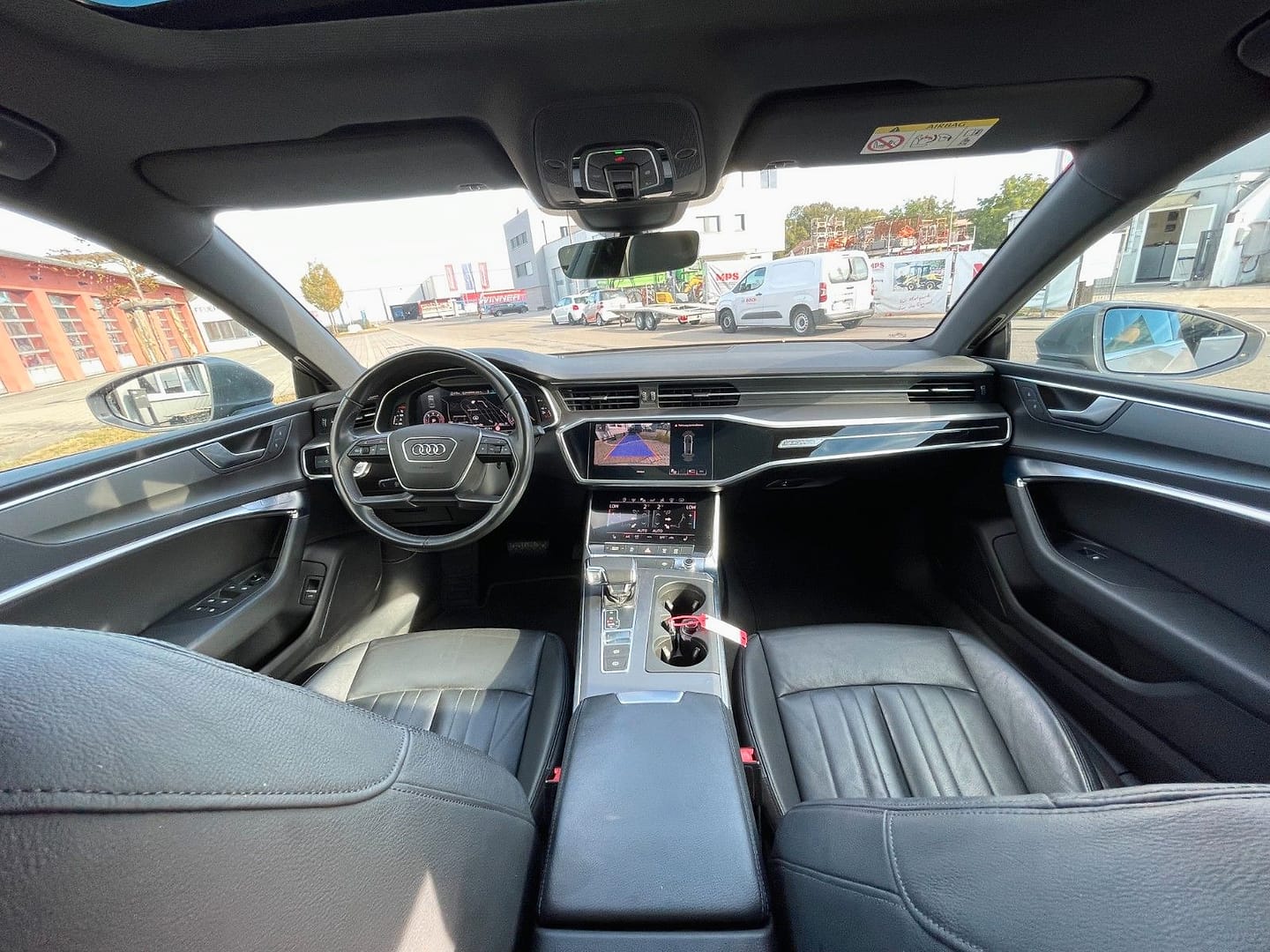 Blick von der Rückbank nach vorn in einen Audi A7: Lenkrad, Kombiinstrument, Bildschirm in der Mittelkonsole und schwarze Ledersitze