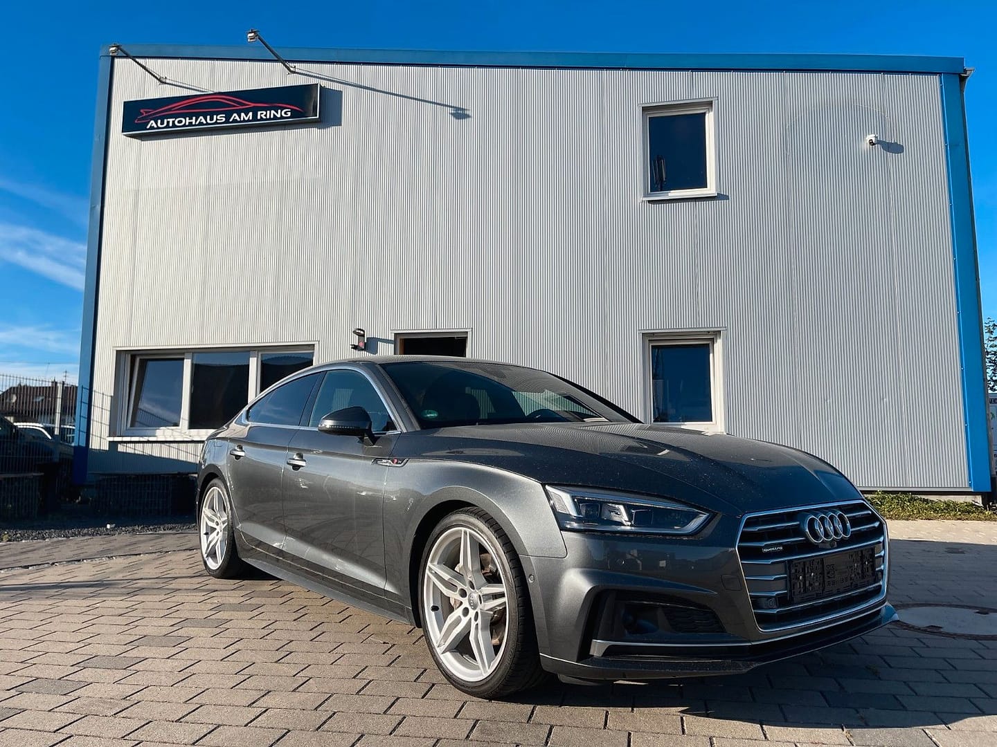 Audi A5 Sportback quattro in Grau, schräg von vorn, vor der Halle in Illingen